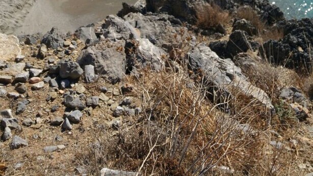 Paesaggio costiero con terreno roccioso, acque cristalline turchesi e una spiaggia sabbiosa.