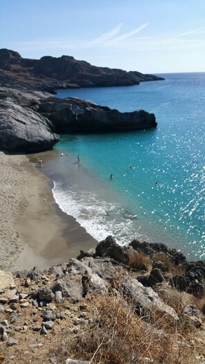 Un paysage côtier caractérisé par un terrain rocheux, des eaux turquoise et limpides, et une plage de sable.