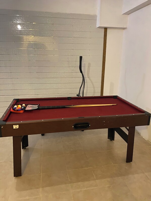 Une table de billard avec des billes et des queues, un mur avec des lignes horizontales et une lampe.