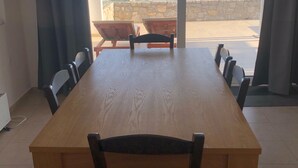 Zona pranzo con un grande tavolo di legno e sei sedie, vista mare attraverso ampie finestre e un muro in pietra all'esterno.