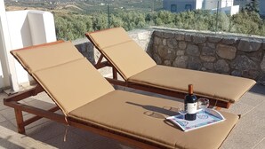 Due lettini con cuscini beige su un patio piastrellato con vista su un paesaggio montuoso.