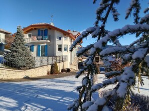 Un edificio residenziale con un balcone, un muro in pietra e terreno innevato.
