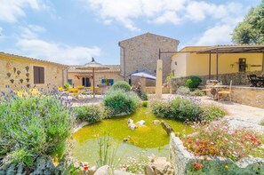 A courtyard with a pond, stone buildings, and outdoor seating.