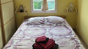 A bed with a patterned bedspread, a window with curtains, a bedside lamp, and a small shelf with a lantern.