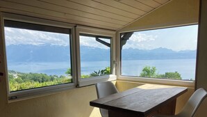 A room with a wooden table and two chairs, large windows with a view of mountains and a lake.