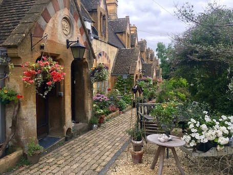 Una calle adoquinada flanqueada por edificios históricos, cada uno decorado con cestas de flores colgantes y macetas.