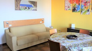 Una habitación con un sofá color beige, una mesa redonda con mantel estampado y un cabecero de madera.