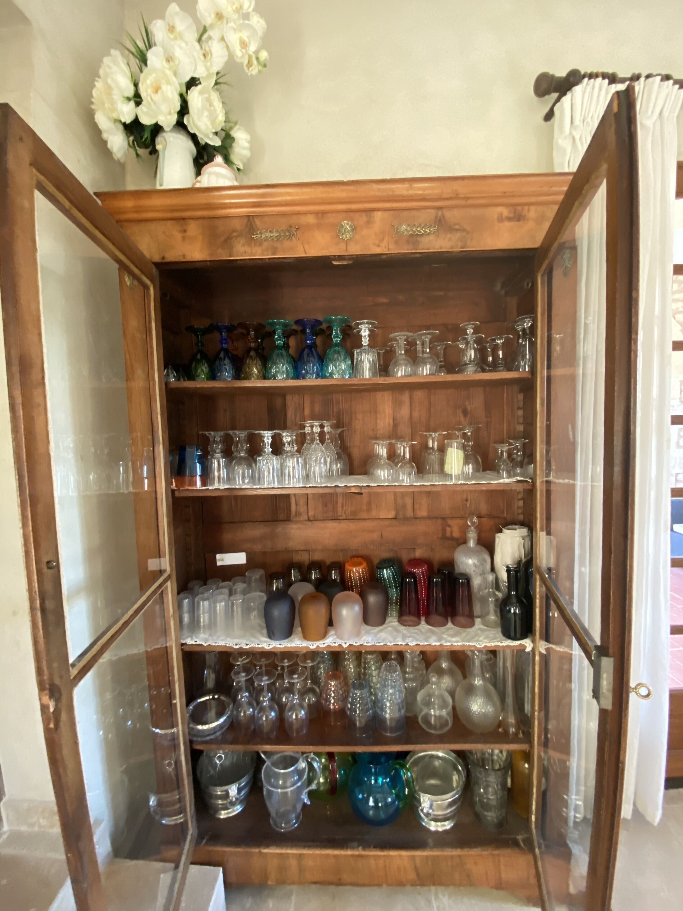 A wooden cabinet with glass doors displaying various glassware and decorative items.