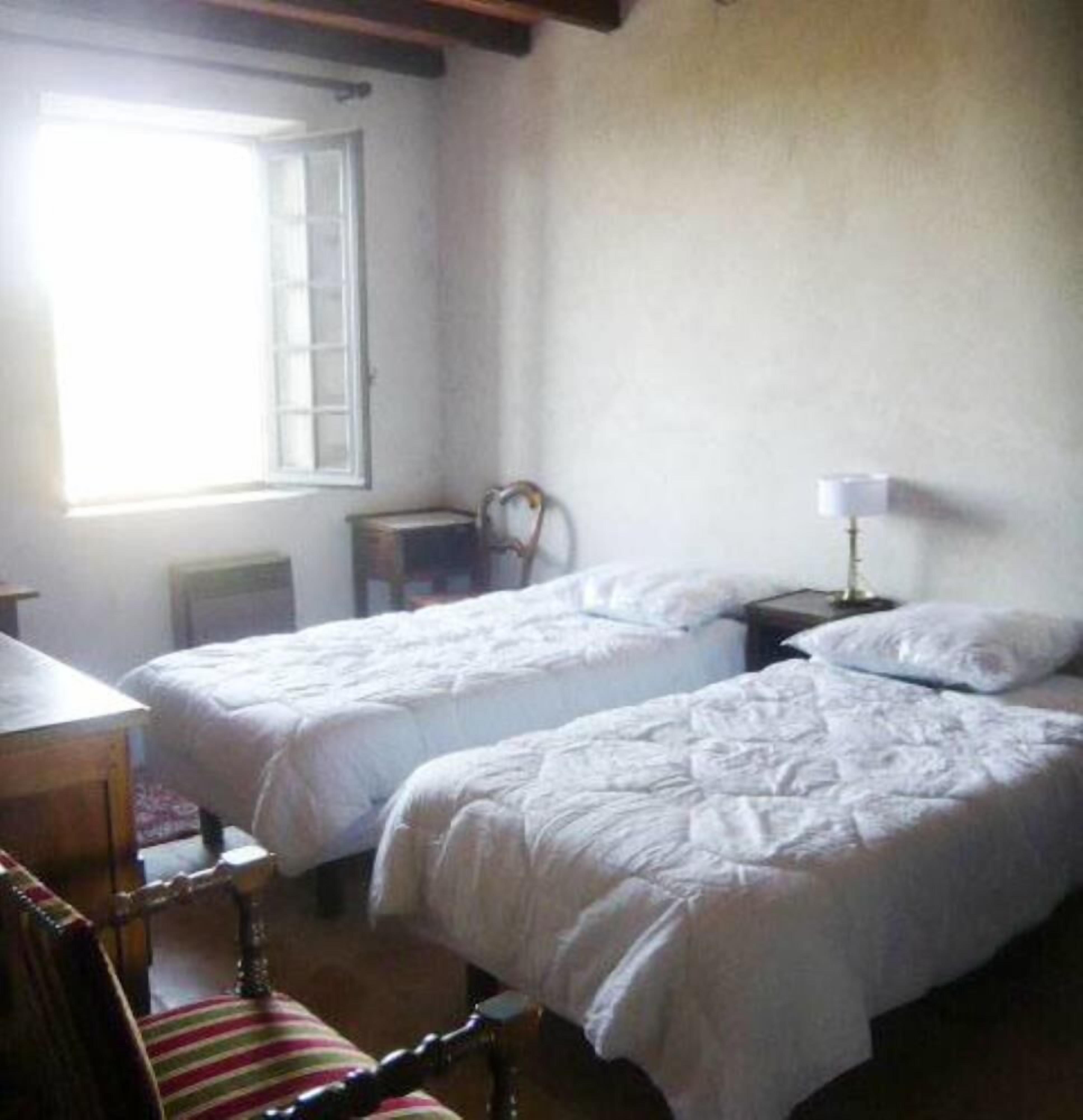Una habitación con dos camas, una silla, una mesa y una ventana.