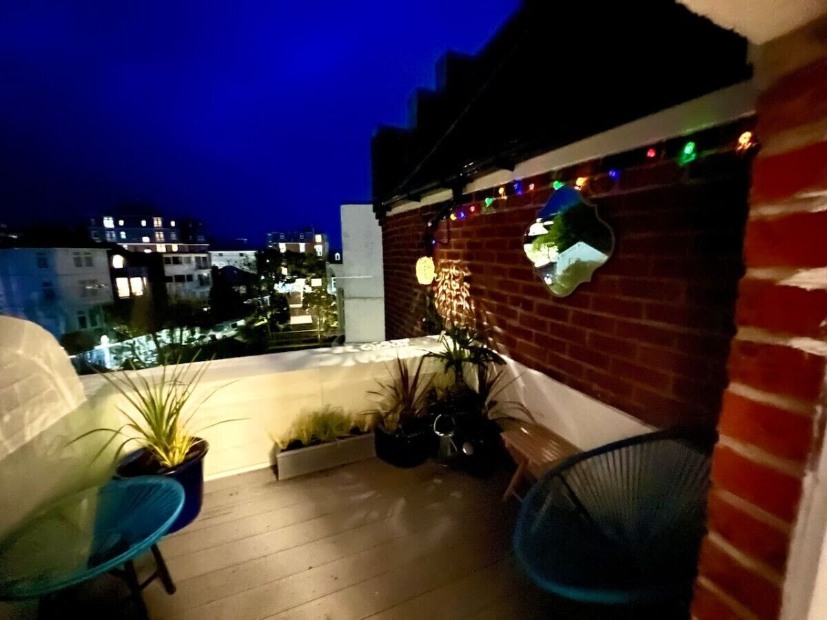 A rooftop terrace with a brick wall, potted plants, and string lights.