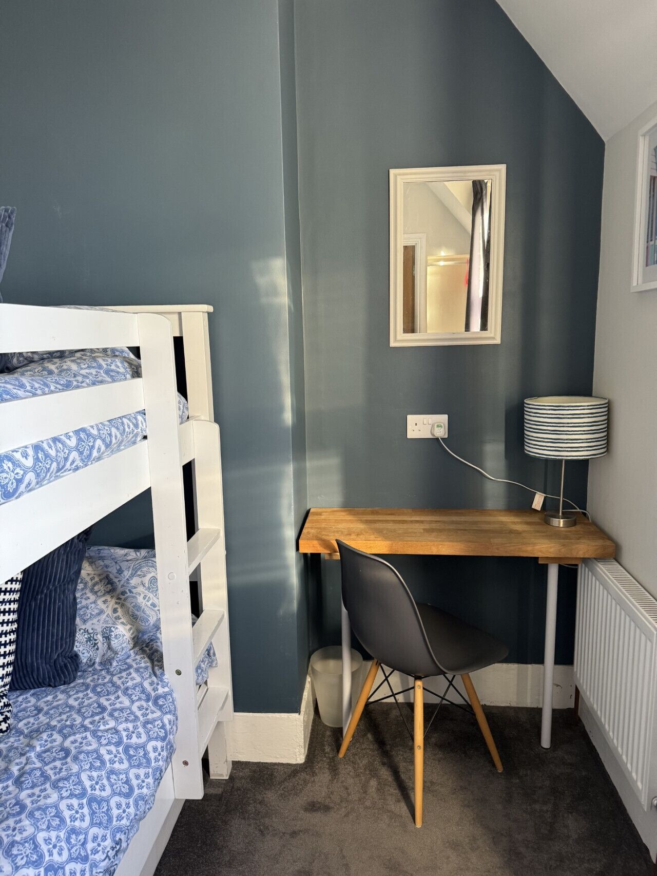 A bedroom with a bunk bed, a desk with a chair, a mirror, and a lamp.