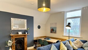 A living room with a fireplace, blue sofa, dining table, and a large window. - Roof Terrace Beach at end of road, Private Parking (Portsmouth)