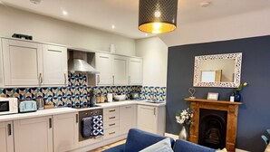 A modern kitchen with white cabinets, a patterned backsplash, and a blue sofa with cushions. - Roof Terrace Beach at end of road, Private Parking (Portsmouth)