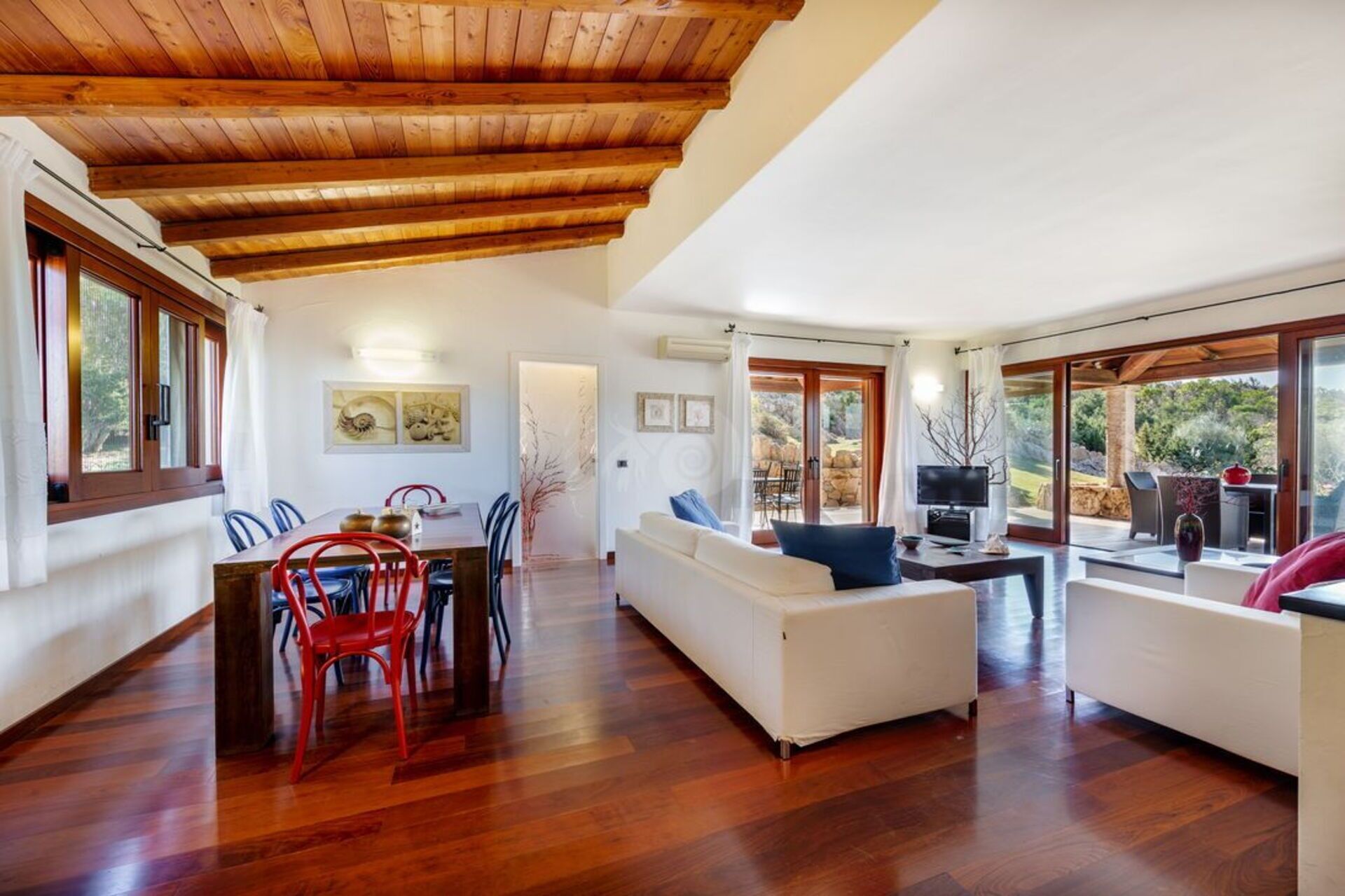 Un amplio salón con techo de madera, una mesa de comedor con sillas, un sofá y un televisor.