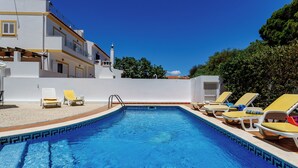 Une piscine à l’eau d’un bleu cristallin, entourée de bâtiments blancs aux contours jaunes et dotée d’une terrasse carrelée.