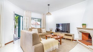 Un salon comprenant un canapé, une table basse, un téléviseur, une cheminée et une vue sur l’extérieur, visible à travers une porte vitrée.