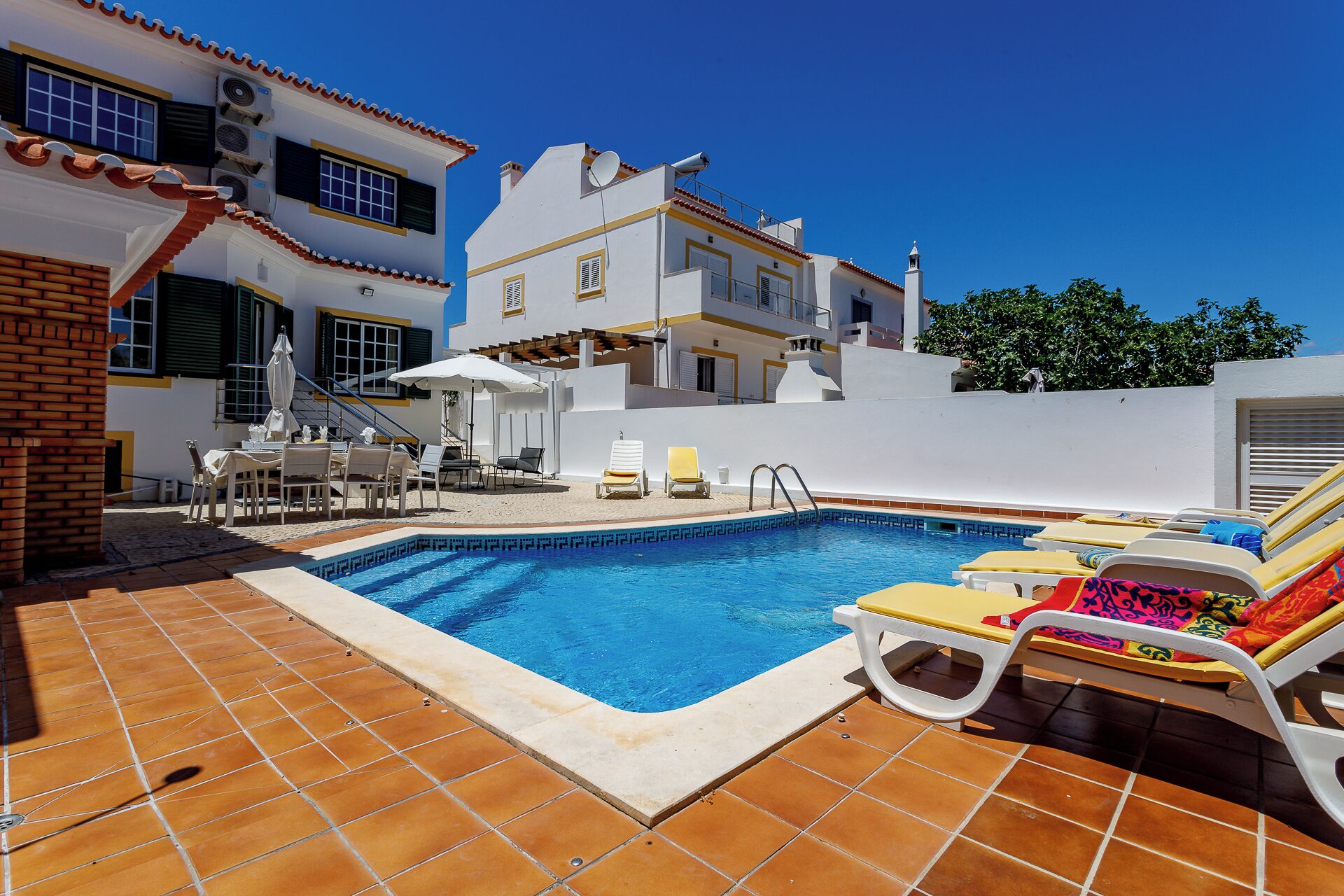 A swimming pool with lounge chairs, a table with chairs, and a staircase leading to an upper level.