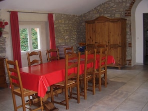 A dining room with a long table covered in a red tablecloth, surrounded by wooden chairs. There is a stone wall and a wooden cabinet in the background. - cottage 8 people 4 bedrooms 3 stars in a farmhouse surrounded by vineyards (Saint-Hilaire-De-Brethmas)