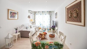Ein Essbereich mit Tisch, gedecktem Tisch für eine Mahlzeit, einer Couch und einem Fenster mit blumigen Vorhängen.