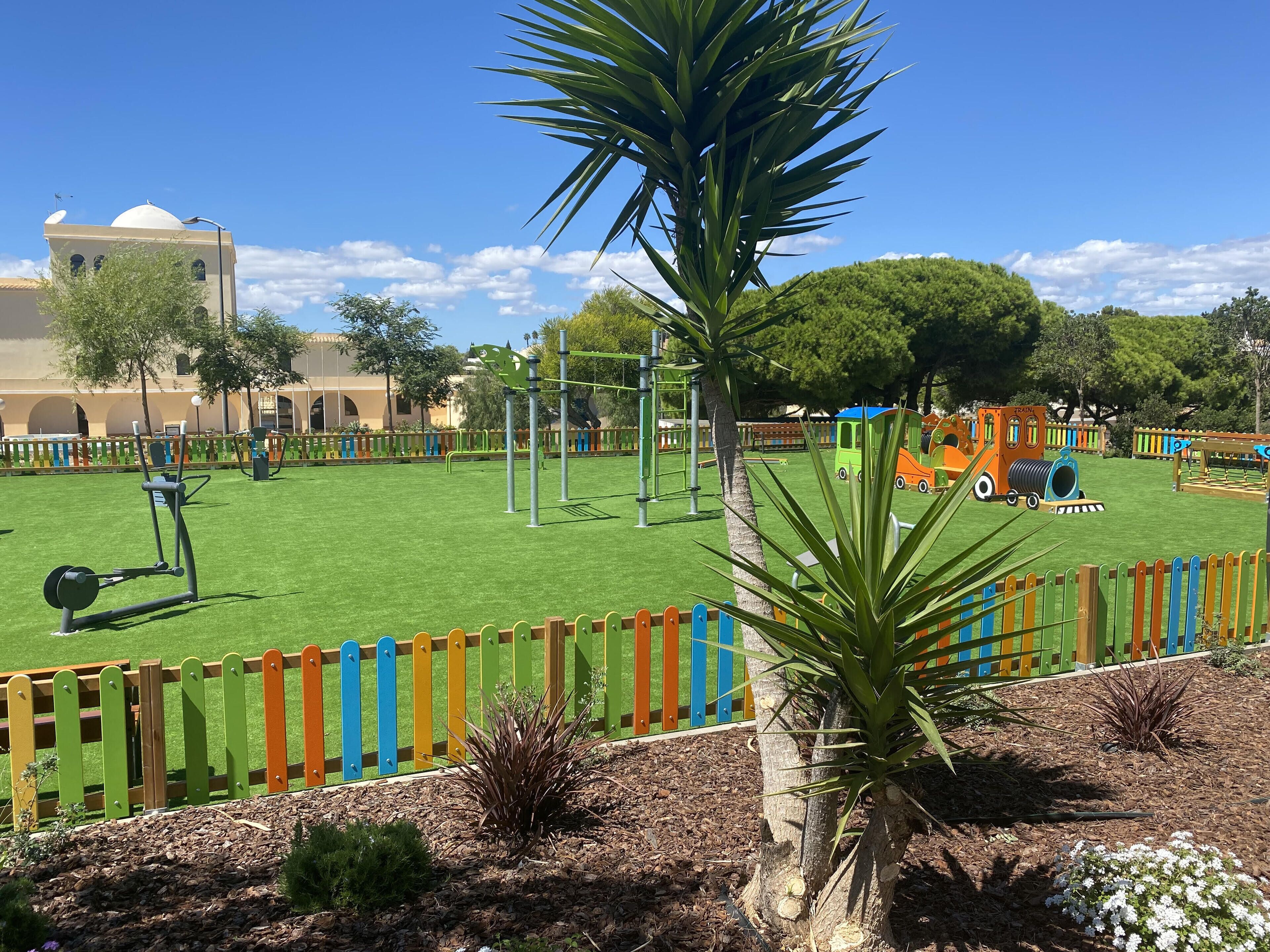 A playground with exercise equipment, a colorful fence, and a building in the background.