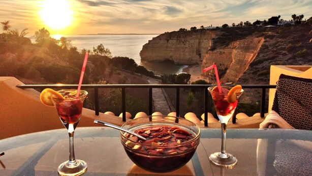 Ein Tisch mit zwei Getränken und einer Schüssel Essen, mit Blick auf eine Küstenlandschaft mit Klippen und dem Meer.