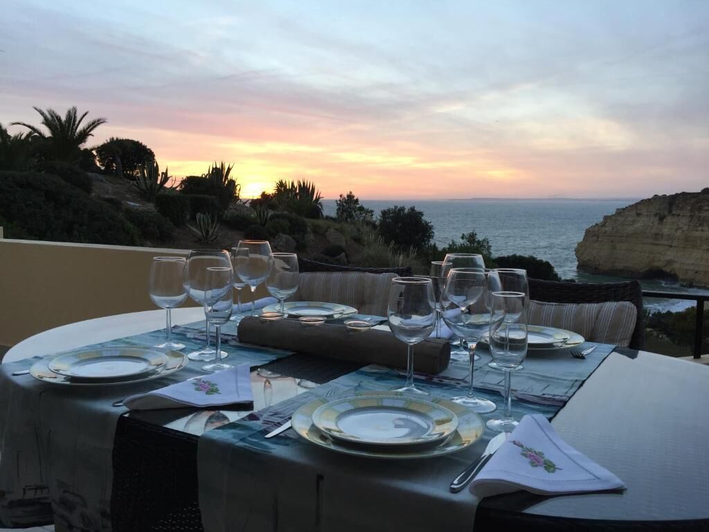 A table set for dining with a view of the ocean and cliffs at sunset.