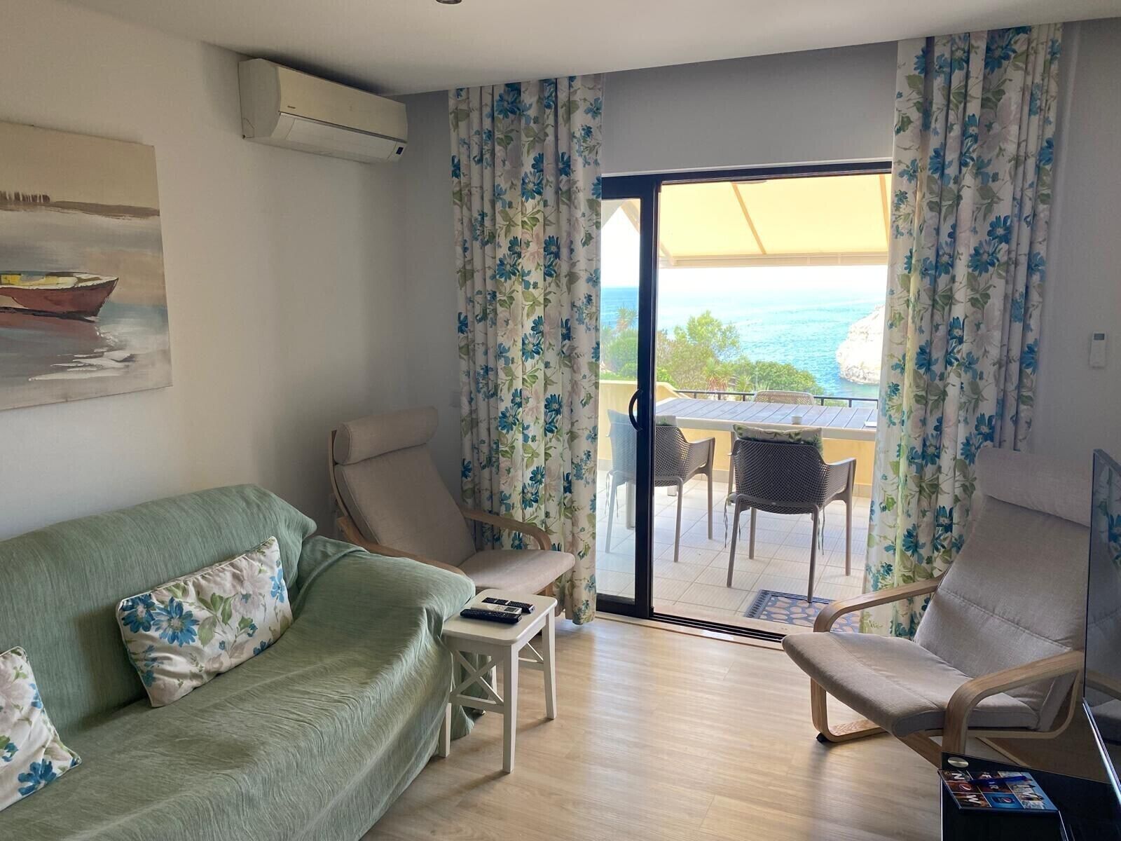 A living room with a sofa, chairs, a small table, and a view of the sea through a glass door.