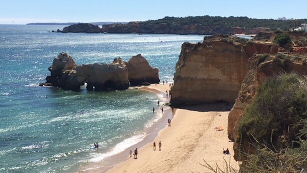 Uma praia costeira com formações rochosas e água azul cristalina.