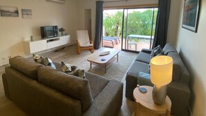 Uma sala de estar com sofá, mesa de centro, televisão, poltrona e luminária.