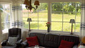 A living room with a leather sofa, a leather armchair, a round coffee table, and a view of a green lawn through large windows.