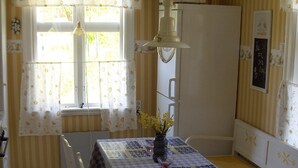 A dining area with a table set for two, a white refrigerator, and a window with curtains.