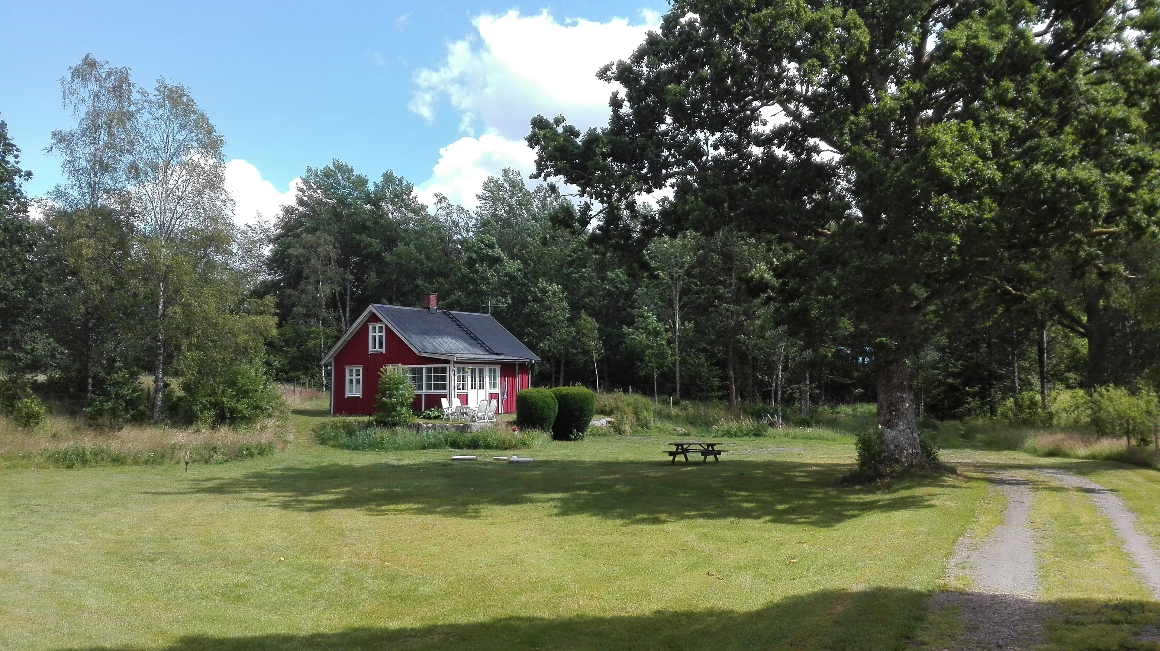A red house with a porch and a picnic table in a grassy area with trees.