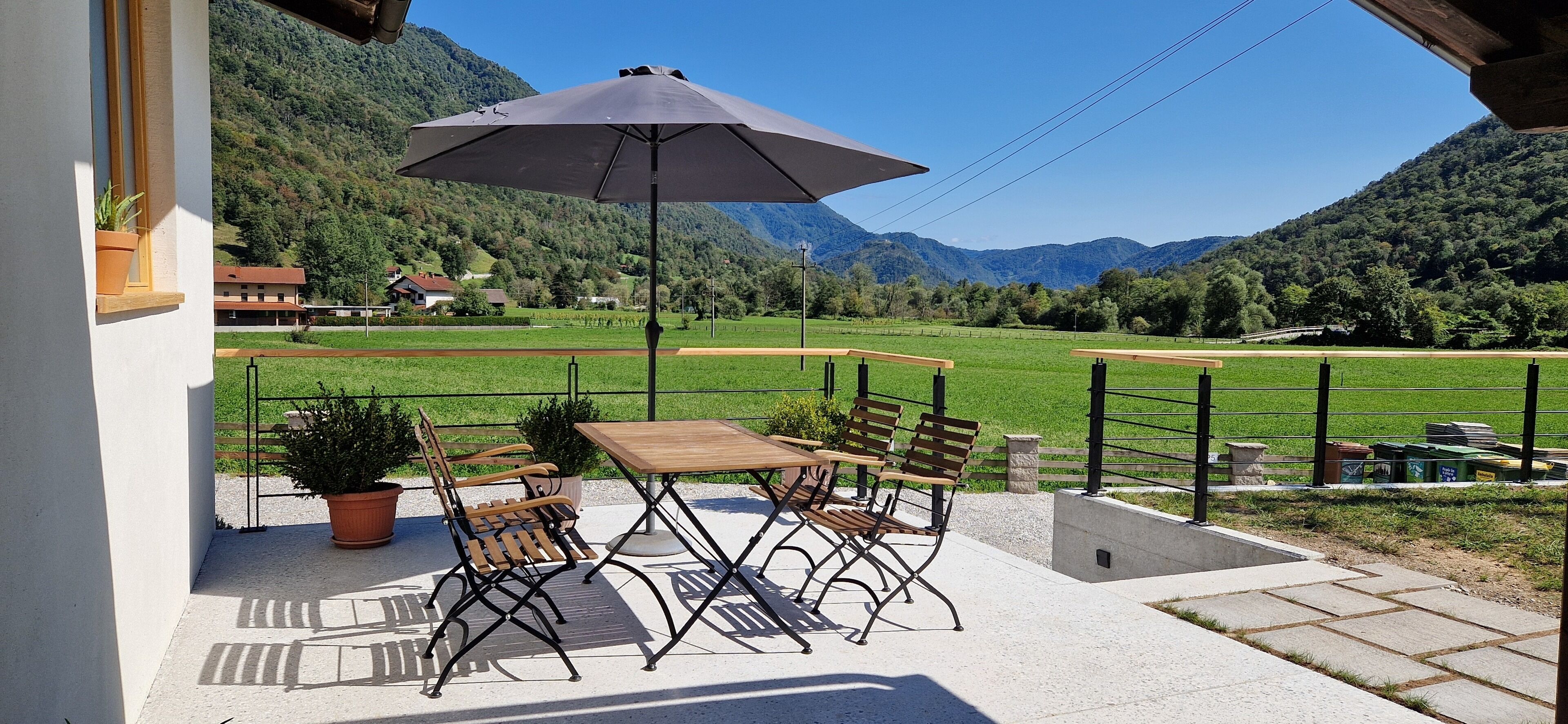 Eine Terrasse im Freien mit Tisch, Stühlen, einem Blumentopf und einem großen Sonnenschirm.