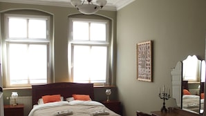 Une chambre à coucher avec un grand lit, un bureau en bois, une chaise, une commode et un ventilateur de plafond.