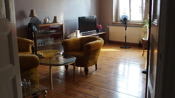 Un salon avec un plancher en bois, un fauteuil jaune, une table basse en verre, un téléviseur et une bibliothèque.