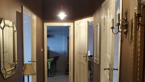 Un couloir avec un sol carrelé, une lampe, un miroir et un vase rempli de fleurs.