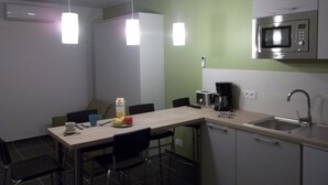 Eine kompakte Küche mit Mikrowelle, Kaffeemaschine und Toaster. Es gibt Stühle und einen Tisch mit Milchkarton und Obst.