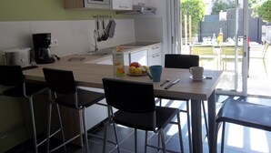 Eine moderne Küche mit Mikrowelle, Toaster und Kaffeemaschine. Vier Stühle um einen Tisch, auf dem sich eine Obstschale und eine Tasse befinden.