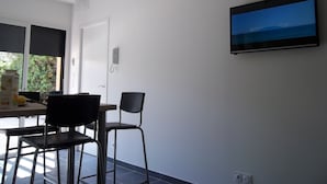 Ein Zimmer mit Esstisch, zwei Stühlen, einem flachbildfernseher an der Wand und einem Fenster mit Jalousien.