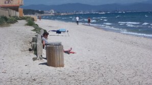 Ein Strand mit einem Gebäude, einer Mülltonne und einer Person, die im Sand liegt.