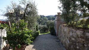 A gravel path leading to a stone wall with a potted plant and two spherical street lamps.