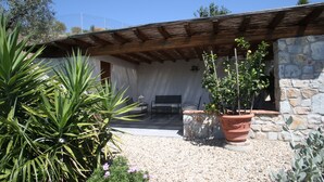A patio with a stone wall, a wooden pergola, and potted plants.