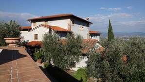 A white building with a red-tiled roof, surrounded by olive trees and a clear sky.
