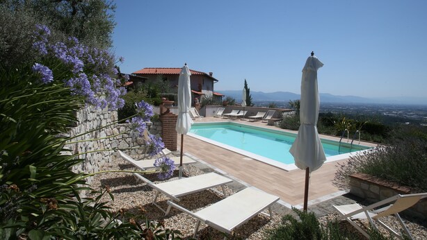 A pool area with lounge chairs and umbrellas, surrounded by stone walls and vegetation.