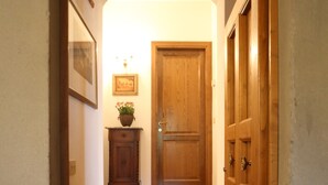 A hallway with a wooden door, a small cabinet with a plant, and a tiled floor.