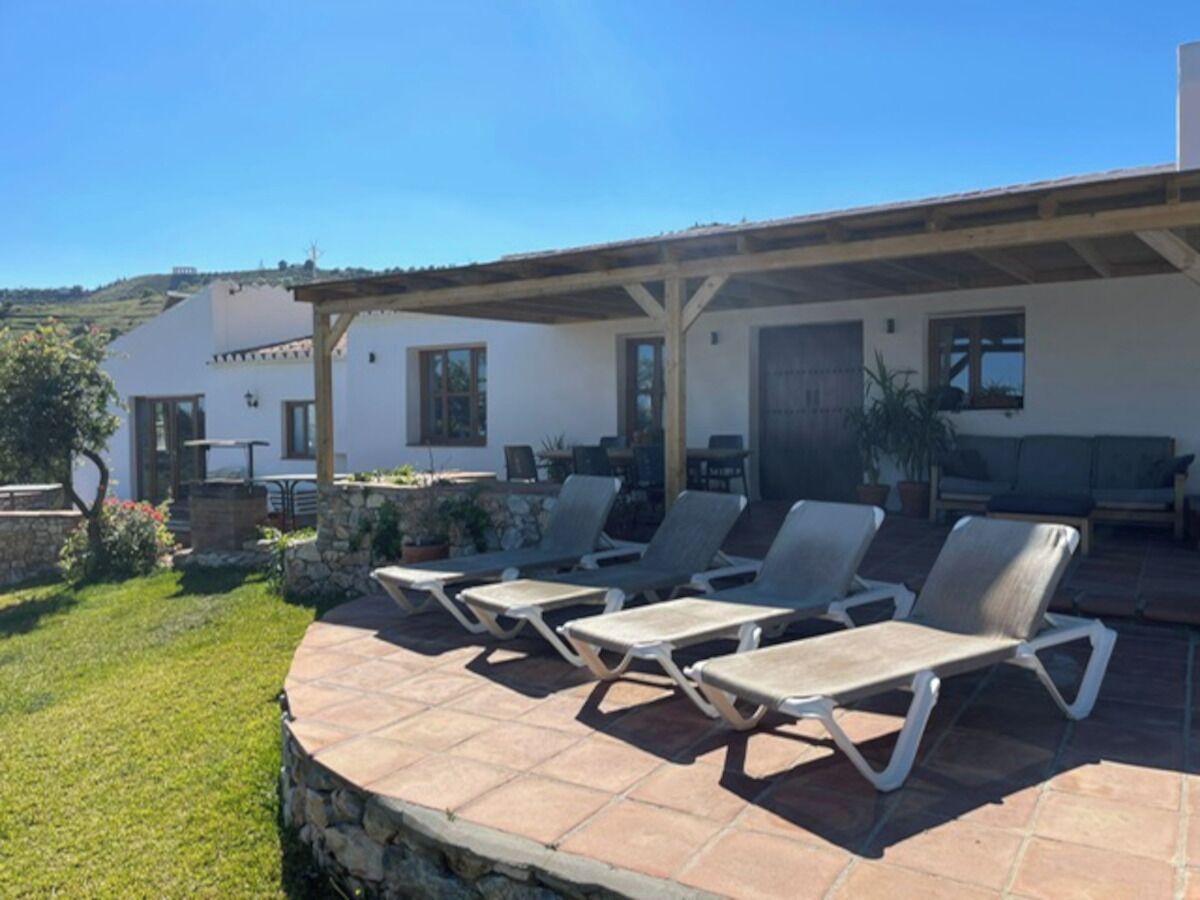 Une terrasse avec des chaises longues, un espace salon couvert et un mur en pierre.