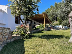 Ein weißes Gebäude mit einer Steinmauer, einer Holzpergola und einem Baum im Vordergrund.