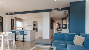 Un salon moderne avec un canapé bleu, une table basse en verre et un coin repas avec des chaises blanches.