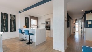 Une cuisine moderne avec des meubles blancs, un îlot central doté de tabourets de bar et un micro-ondes visible.