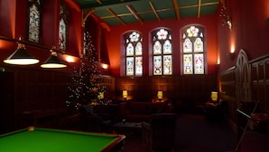 A billiards room with a green pool table, a Christmas tree, and stained glass windows.